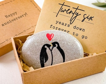 May include: A decorative stone with two painted penguins kissing under a red heart, presented in a small brown box. The box contains a card that reads "twenty six years down forever to go". A second box reads "Happy anniversary!"