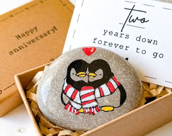 May include: A small gift box with a hand-painted stone featuring two penguins wearing a red and white scarf. The box also includes a card that reads "Two years down forever to go".