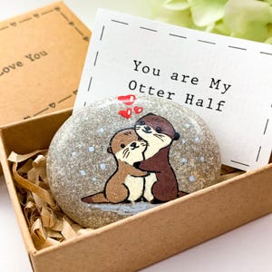 Pu&ograve; includere: Un sasso dipinto con due lontre che si abbracciano, con cuori rossi sopra, all'interno di una scatola marrone. Una carta con la scritta "You are My Otter Half" &egrave; dietro la pietra. La scatola &egrave; in una scatola pi&ugrave; grande con "I Love You".