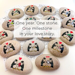 May include: Hand-painted stones with penguin couples, hearts, and gifts. The text on the stones reads "One year. One stone. One milestone in your love story." Ideal for anniversary gifts. Each stone is unique.