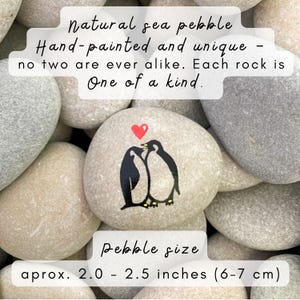 May include: Hand-painted natural sea pebble with a black and white penguin design and a red heart. The pebble is approximately 2.0 - 2.5 inches in size. The text on the image says "Natural sea pebble, Hand-painted and unique - no two are ever alike. Each rock is One of a kind."