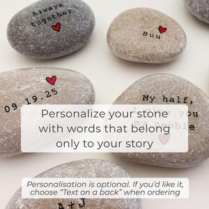 May include: A collection of smooth, gray and tan river stones, each inscribed with personalized text and a small red heart. The stones feature phrases like "Always together" and "My half," with the option for custom text.