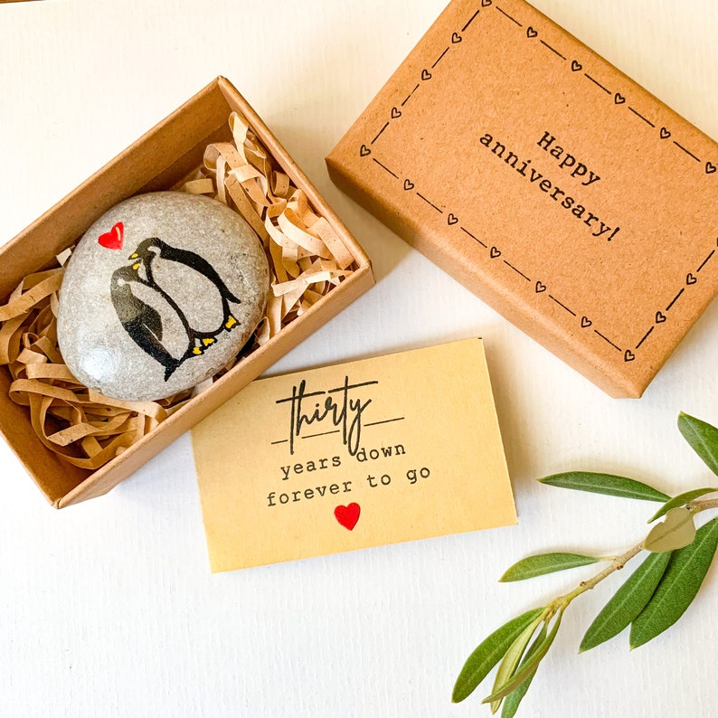 May include: A small, brown box with a white painted penguin couple on a stone inside. The box has a card that reads "Thirty years down forever to go" with a red heart. The box lid has the text "Happy anniversary!" with a border of hearts.