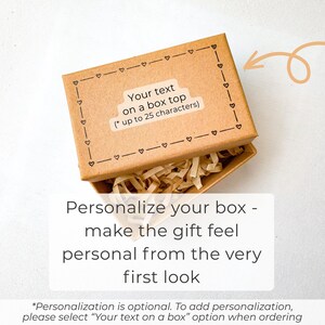May include: A rectangular brown cardboard gift box with a lid featuring a black printed border of small hearts and the text "Your text on a box top (* up to 25 characters)". The open box contains light tan shredded paper filler material.