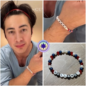 Op de afbeelding: Een armband met witte letterkralen met de tekst "HOLLANOV" en rode, witte en blauwe kralen. De armband wordt om een pols getoond en ook apart weergegeven. De afbeelding bevat een persoon die de armband draagt.