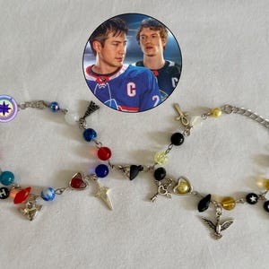 May include: Two beaded bracelets with silver chains and various charms. One bracelet features red, blue, and turquoise beads with charms including a star, heart, and an angel. The other bracelet has black, yellow, and clear beads with charms like a key and a dove.