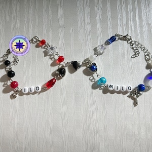 May include: Two friendship bracelets with the names "ILO" and "MILO" spelled out in white beads. The bracelets are made with silver chain, black, red, blue, and white beads, and silver heart charms.