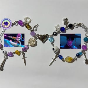 May include: Two beaded bracelets with silver chains and charms. One bracelet features a picture of a woman with purple hair, purple and yellow beads, and a cross charm. The other bracelet has a picture of a man, blue and yellow beads, and a skull charm.