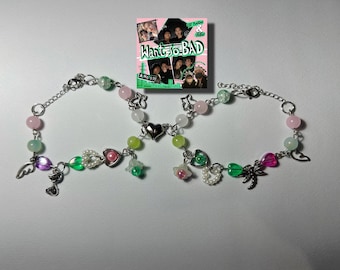 May include: Two silver charm bracelets with green, pink and white beads. The charms include a heart, a flower, a dragonfly and a wing. The bracelets are connected by a silver heart charm.