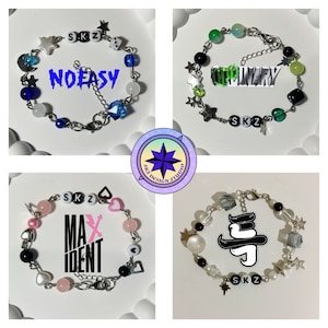 Puede incluir: Cuatro pulseras con diferentes dijes y cuentas. Las pulseras tienen el texto "SKZ", "NOEASY", "ODINARY", "MAXIDENT".