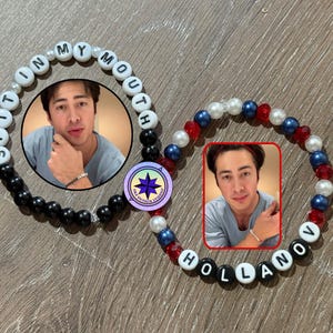 May include: Two beaded bracelets with the text "SPIT IN MY MOUTH" and "HOLLANOV" spelled out in white letter beads. One bracelet features a photo of a person. The other bracelet has red, white, and blue beads.