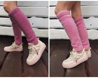 May include: A pair of pink fuzzy leg warmers worn over white sneakers with a pink sole. The leg warmers are made of a soft, fluffy material and are a great way to add a touch of warmth and style to any outfit.