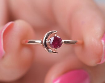 Könnte beinhalten: Ein Ring aus Roségold mit einem Halbmond-Design und einem roten Edelstein in der Mitte.