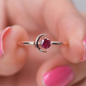 May include: A rose gold ring with a crescent moon design and a red gemstone in the center.