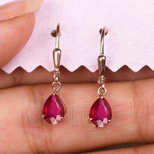 May include: A pair of gold earrings with teardrop-shaped red ruby stones.