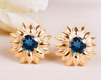May include: A pair of gold sunflower earrings with blue gemstone centers.