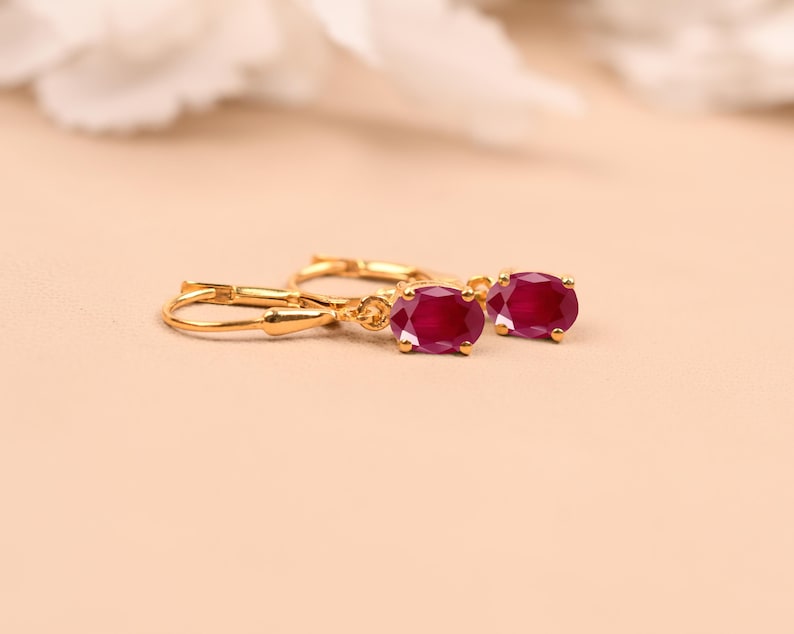 May include: A pair of gold hoop earrings with red oval-shaped gemstones.