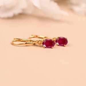 May include: A pair of gold hoop earrings with red oval-shaped gemstones.