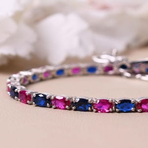 May include: A silver bracelet with alternating blue and pink oval-shaped gemstones.