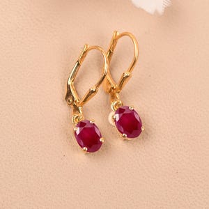 May include: A pair of gold earrings with red oval-shaped gemstones. The earrings have a lever back closure.