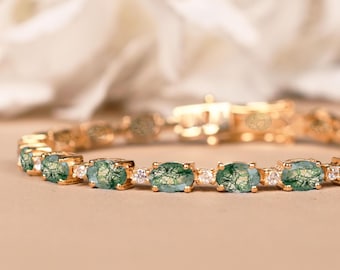 May include: Gold-toned bracelet featuring oval-cut green gemstones with intricate patterns, interspersed with small, clear gemstones. The bracelet is set against a soft, neutral background, highlighting the jewelry's details.