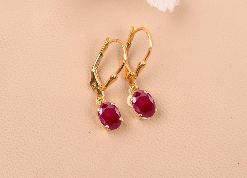 May include: A pair of gold earrings with red oval-shaped gemstones. The earrings have a lever back closure.