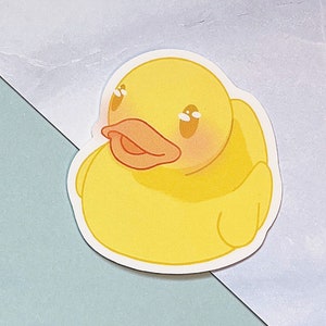 May include: A yellow rubber duck with a wide, orange beak and closed eyes. The duck has a blush on its cheeks and a white outline.