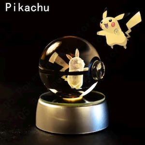 May include: A clear glass sphere with a Pikachu design inside, illuminated by a light on a silver base. The word "Pikachu" is at the top left. A yellow Pikachu graphic is to the right.