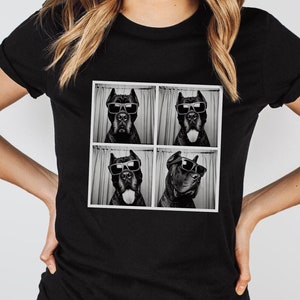 May include: Black t-shirt with a photo of a dog wearing sunglasses in a photo booth. The dog is in four different poses.