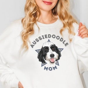 May include: White sweatshirt with a blue and gray star design featuring a black and white doodle dog. The text "AussieDoodle Mom" is printed on the sweatshirt.