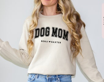 Könnte beinhalten: Ein beiger Pullover mit dem Text "DOG MOM" in schwarzen Blockbuchstaben. Unter dem Text steht "BENJI ♥ BAXTER" in kleineren schwarzen Buchstaben.