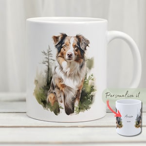 May include: White ceramic mug featuring a watercolour illustration of an Australian Shepherd dog sitting in a woodland scene. The dog is brown, white and black with blue eyes. The mug has a handle and is suitable for hot drinks.