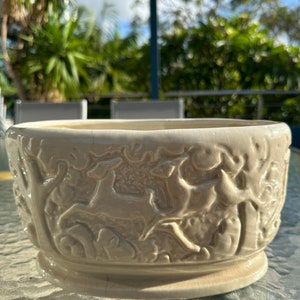 May include: A white ceramic planter featuring a raised design of deer in a woodland scene.