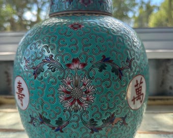 May include: A teal blue ceramic jar with a lid, decorated with intricate floral patterns and Chinese characters. The jar has a gold trim and a yellow base.