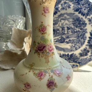 May include: A vintage ceramic vase with a delicate floral pattern in shades of pink, green, and blue. The vase has a bulbous base and a slender neck with a gold rim.