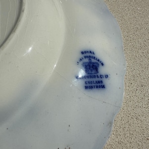 Puede incluir: Un plato de porcelana blanca con un dise&ntilde;o floral azul y un borde festoneado. El plato tiene un sello azul que dice "Royal Porcelain J.A. Wood & Co Ltd England Montrose."