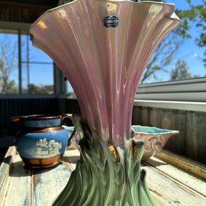Puede incluir: Un jarrón vintage de cerámica iridiscente rosa y verde con detalles dorados. El jarrón tiene una abertura ancha y acampanada y una base que se asemeja a una flor estilizada. El jarrón está etiquetado con "Ceramics Royale" en el lateral.