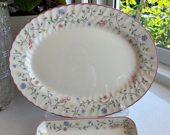 May include: A white oval serving platter with a floral design in shades of pink, blue, and yellow. The platter has a scalloped edge and a pink rim. A smaller rectangular dish with a similar floral design is also included.