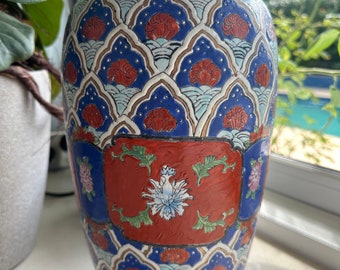 May include: A tall, blue and white ceramic vase with a red and gold floral design. The vase has a rounded body and a narrow neck.