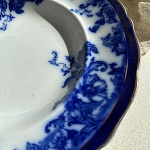 Puede incluir: Un plato antiguo blanco y azul con un dise&ntilde;o floral. El plato tiene un borde azul oscuro con un ribete dorado. El dise&ntilde;o floral es detallado, con un borde festoneado. Di&aacute;metro aproximado de 20 cm.