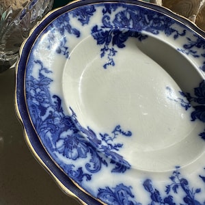 Puede incluir: Plato de servir ovalado antiguo con interior blanco y un patr&oacute;n floral azul. El borde es azul oscuro con un ribete dorado. El plato tiene un asa en un lado y probablemente sea de porcelana.
