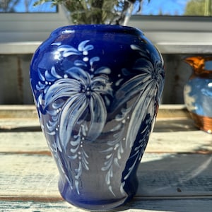 May include: A small, cobalt blue ceramic vase with a white floral design. The vase has a rounded body and a narrow neck.