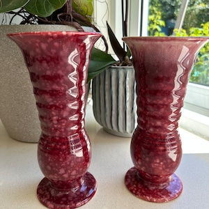 May include: Two red and white ceramic vases with a speckled glaze. The vases have a flared top and a round base.