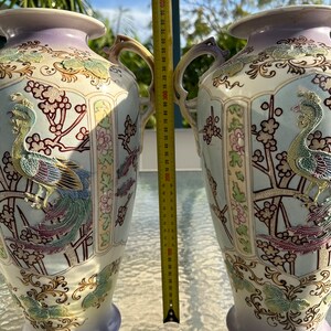 May include: Two ornate ceramic vases with handles, featuring a peacock design in gold, teal, and purple. The vases are approximately 16 inches tall, with a light blue and lavender color scheme, and floral accents.