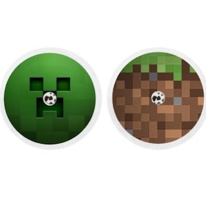 Könnte beinhalten: Zwei runde Aufkleber mit Minecraft-Designs. Ein Aufkleber zeigt ein grünes Creeper-Gesicht mit einem weißen Auge. Der andere Aufkleber zeigt einen braunen Erdblock mit einer grünen Grasdecke.