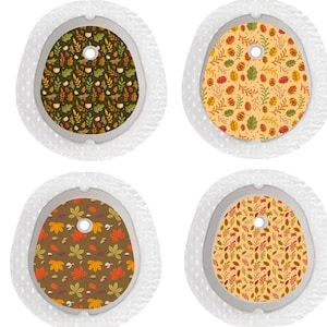 May include: Four adhesive patches for medical devices, each featuring a distinct autumn-themed pattern of leaves, acorns, and small woodland creatures on a textured white backing with a central circular cutout for device sensor access.
