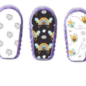 May include: Three purple medical device covers with different designs. One has a white background with daisy flowers, another has a black background with rainbows and clouds, and the last has bees.