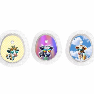 May include: Three decorative cow-themed items. Each has a white, oval-shaped border. The first has a yellow background with a cow wearing sunglasses and a sunflower crown. The second has a holographic background with a cow wearing rainbow sunglasses. The third has a blue sky background with a cow wearing sunglasses.