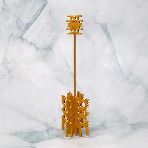 Pode incluir: Um suporte decorativo de metal dourado com um design geométrico. O suporte tem uma coluna alta e fina e uma base de forma circular.