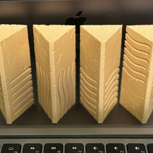 May include: Four beige triangular-shaped columns with different textured patterns. The columns are made of a textured material that resembles stone.